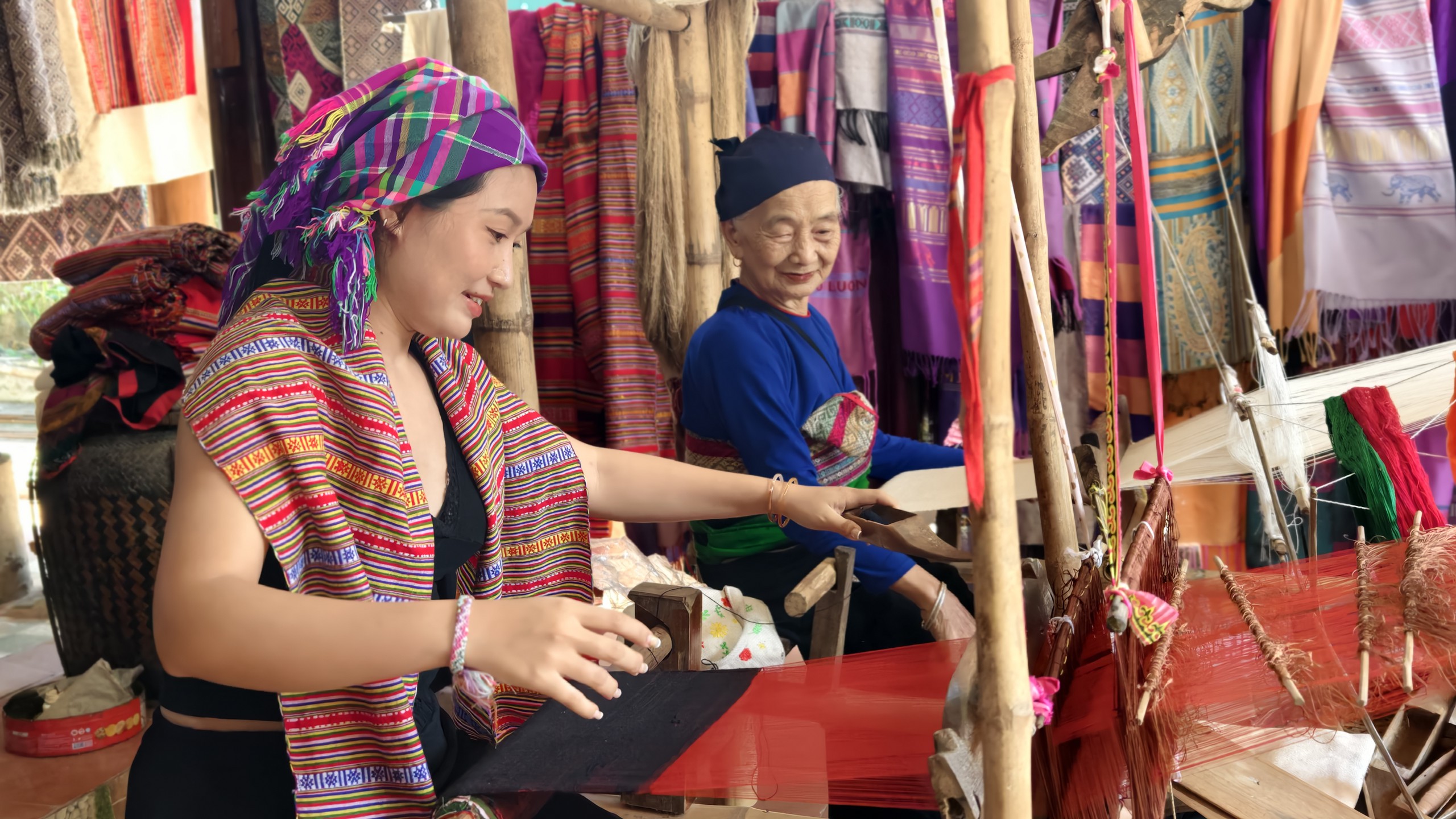 Cụ Hà Thị Nhân hướng dẫn chị Nhân Ái - du khách đến từ TP.HCM dệt vải. Ảnh: Huy Thông - ảnh 1