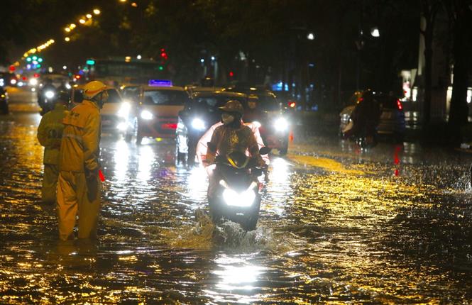 Trong ảnh: Nhân viên thoát nước phân luồng nhắc nhở người tham gia giao thông không đi vào chỗ ngập sâu trên đường Lý Thường Kiệt - Phan Bội Châu. Ảnh: Thành Đạt - TTXVN