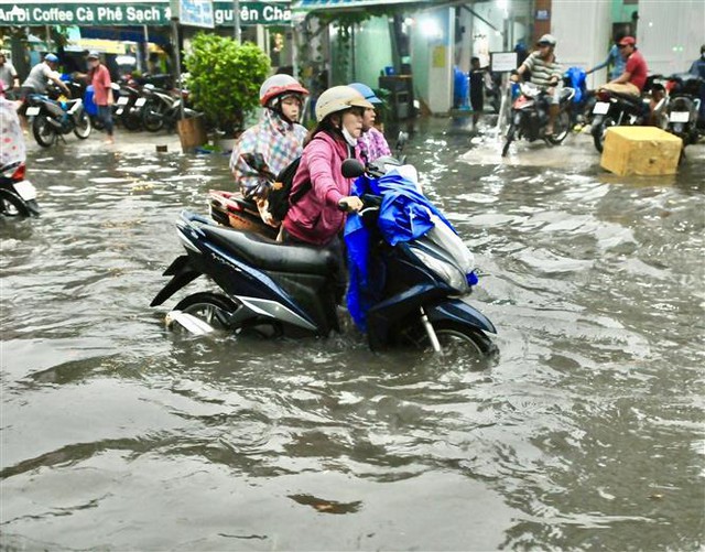Trong ảnh: Nước ngập hơn nửa bánh xe trên đường Huỳnh Tấn Phát (quận 7) khiến người dân phải dắt bộ vất vả. Ảnh: Hồng Giang - TTXVN